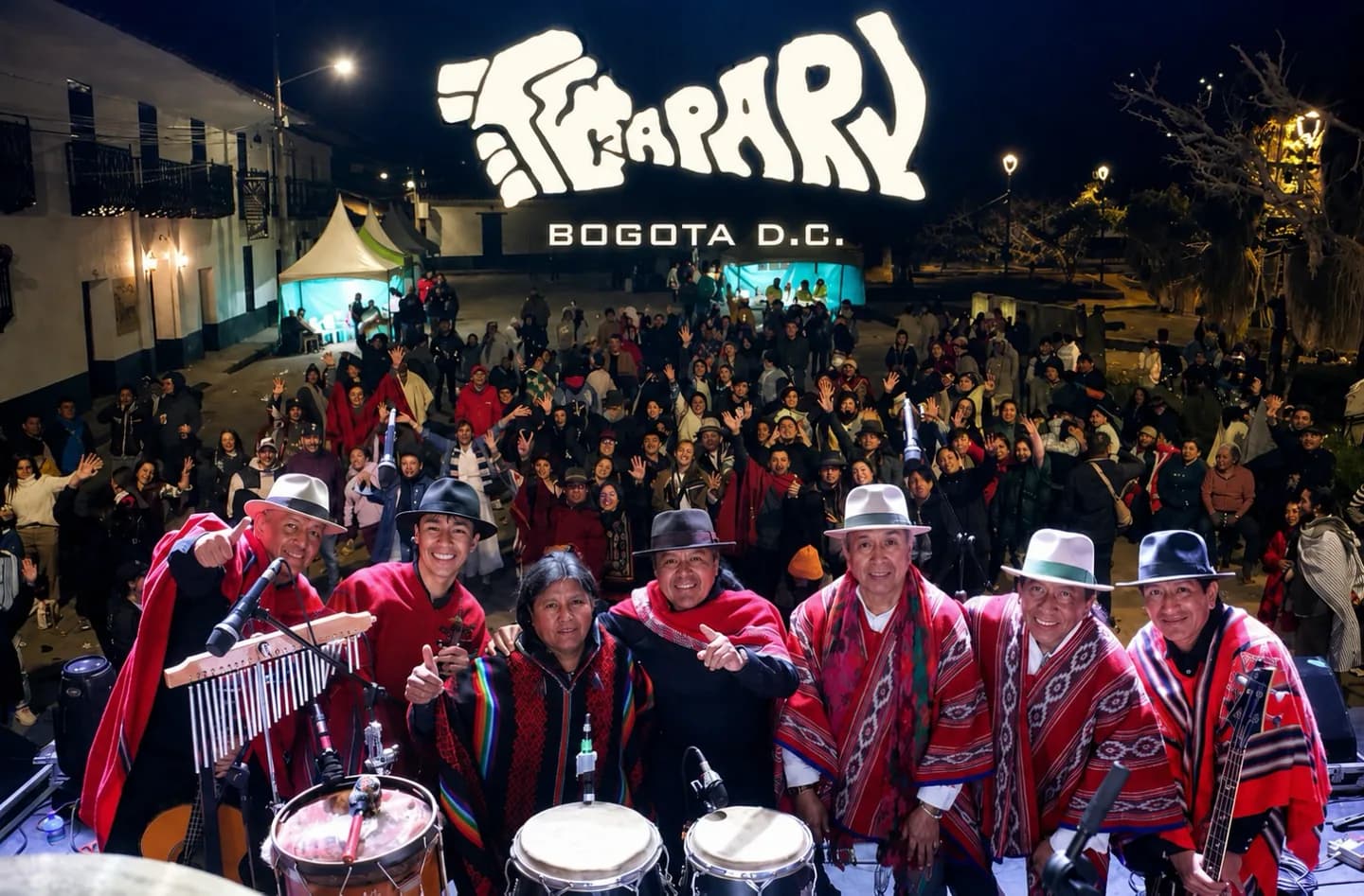 Seven Kapary musicians on stage in Bogotá wearing red woven ponchos